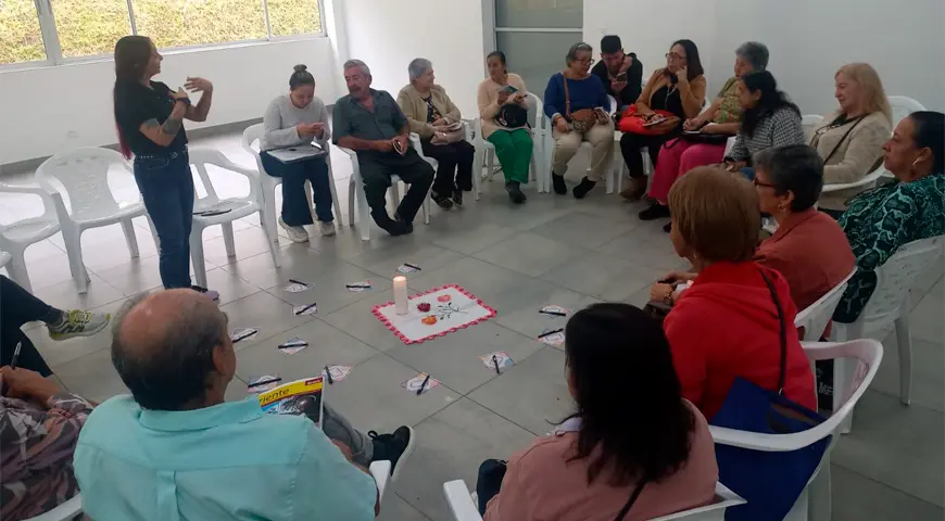 Personas sentadas en un círculo recibiendo una capacitaciòn de una profesora. 