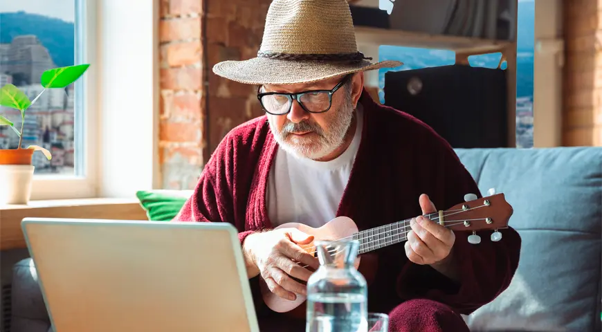 Persona mayor tocando guitarra frente a un computador.